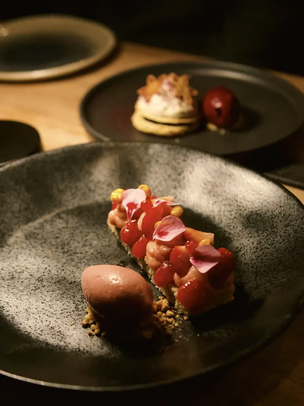 A plated dessert of strawberries and ice cream on dark stoneware