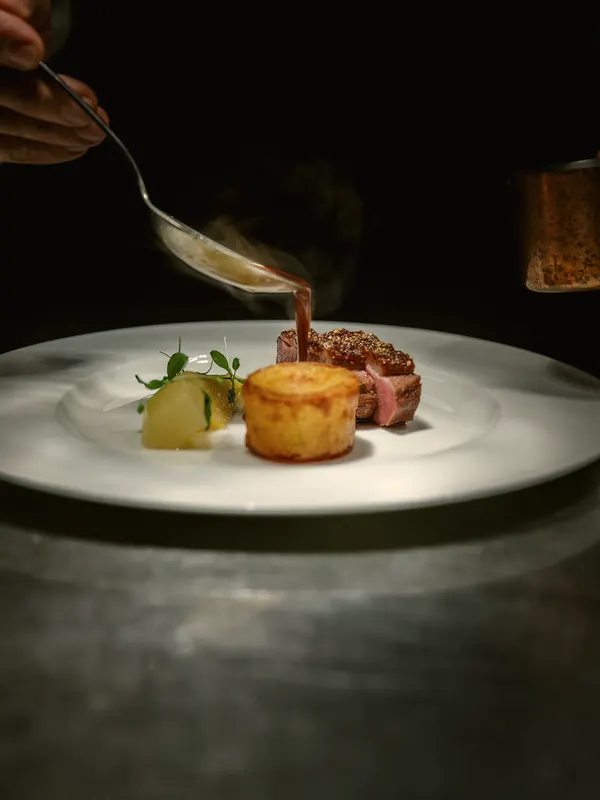 Duck breast with pommes Anna as sauce is poured