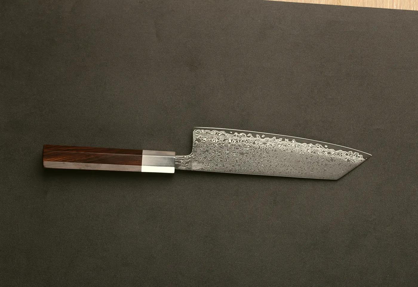 A Damascus-steel kitchen knife resting on a dark board